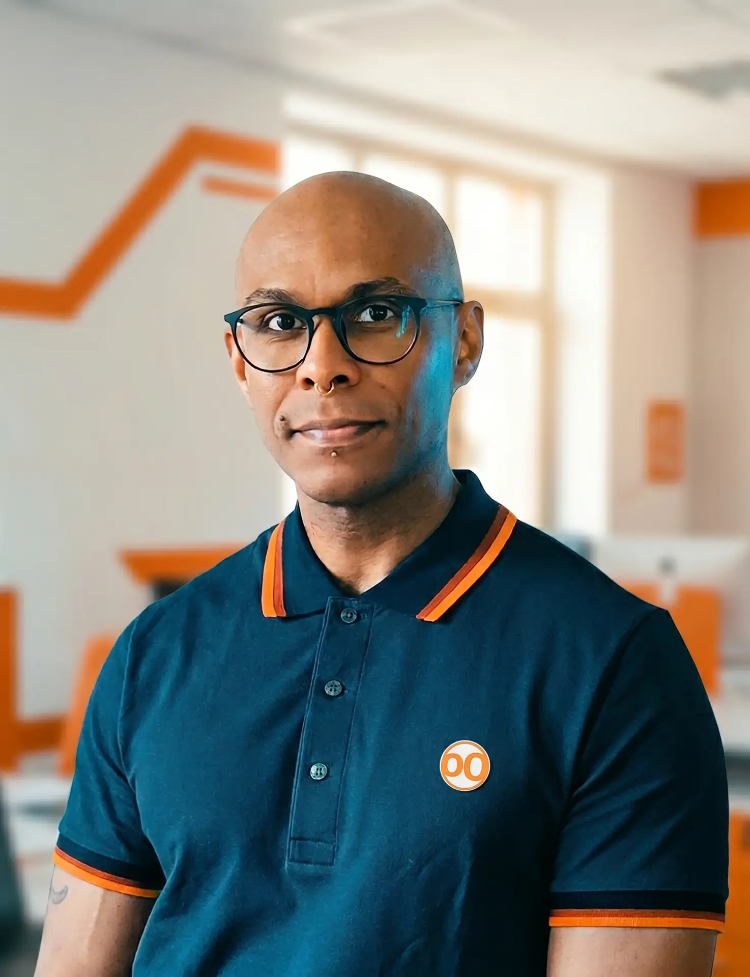 Angelo Oliveira, IT-Berater und Fullstack-Entwickler von UBODA IT-Solutions in Nürnberg, lächelt in einem professionellen Büro-Setting mit orangefarbenen Brand-Elementen.